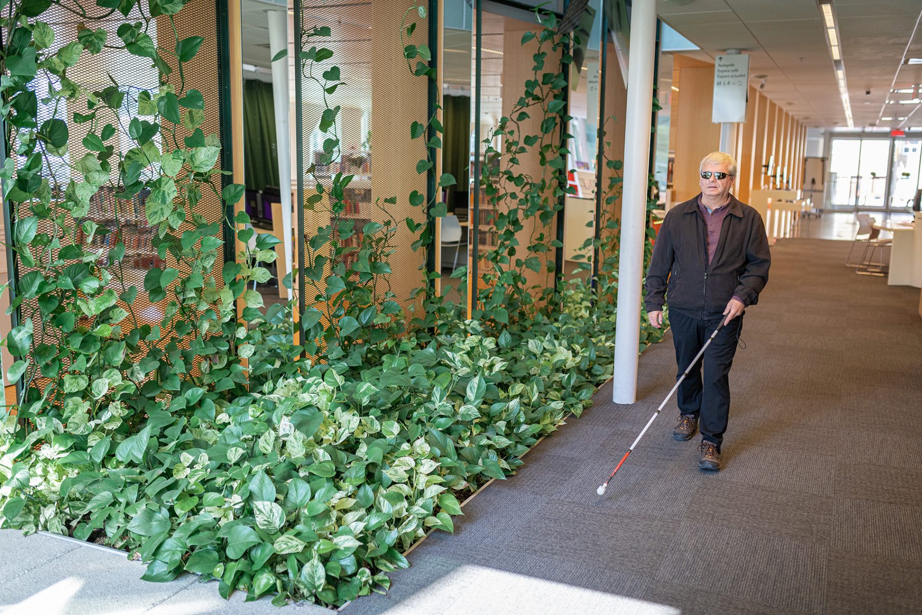 Un homme ayant une déficience visuelle marche avec une canne blanche dans un édifice public.